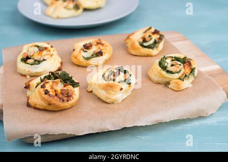 Blätterteig mit Spinat und Feta-Käse, zu Spiralen aufgerollt, frisch aus dem Ofen, blauer Hintergrund Stockfoto