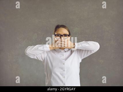 Nahaufnahme einer jungen Frau in einer weißen Bluse in einer Linie, die ihren Mund mit den Händen bedeckt Stockfoto