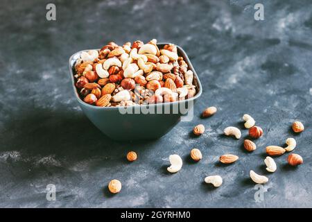 Mischen Sie Walnüsse, Cashewkerne, Haselnüsse und Mandeln in einer Keramikschale auf blauem Betonboden im dunklen Stil Stockfoto