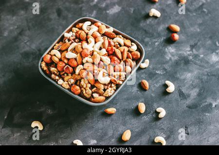 Mischen Sie Walnüsse, Cashewkerne, Haselnüsse und Mandeln in einer Keramikschale auf blauem Betonboden im dunklen Stil Stockfoto