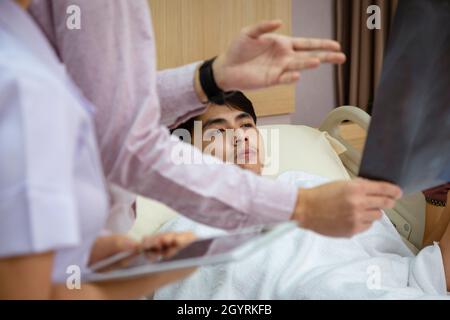 Arzt und Krankenschwester erklären dem asiatischen Patienten im Krankenhaus die Untersuchung des Röntgenfilmergebnisses der Brust und beraten ihn bei der Behandlung. Stockfoto