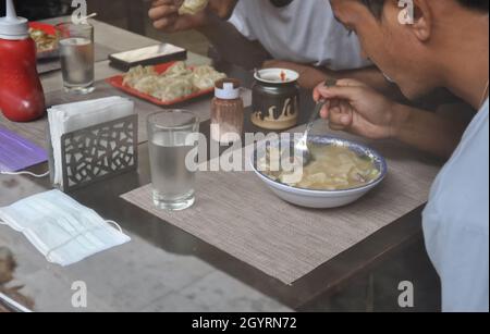 Menschen, die tibetisches Essen in einem Café im Innenbereich essen, das durch das Fenster gesehen wird Stockfoto