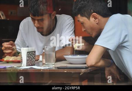 Zwei junge Leute essen Fast Food im Cafe im Innenbereich, das durch das Fenster gesehen wird Stockfoto