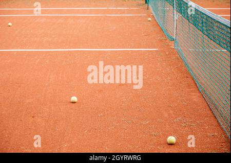 Leerer Tennisplatz aus Lehm. Tennisbälle in der Nähe des Netzes. Weiße Streifen. Trockenes Gras. Stockfoto