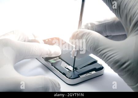 Nahaufnahme von Smartphone-Reparaturtechnikern repariert Mobiltelefone mit einem kleinen Schraubendreher, der in einem weißen Labor mit einem weichen Orange Gummihandschuhe trägt Stockfoto