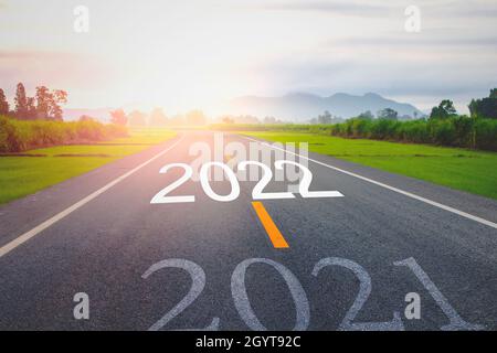 Konzept neues Jahr mit dem Wort 2021 bis 2022 auf der Asphaltstraße in der Landstraße geschrieben Dekorieren Sie orangefarbenes Licht für Schönheit mit Blick auf Reispiel Stockfoto