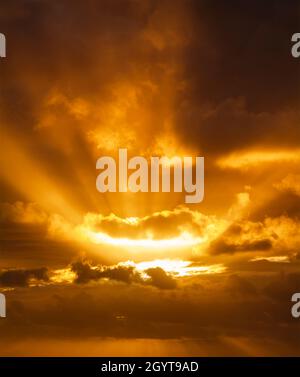 Sonnenstrahlen brechen bei Sonnenuntergang durch die dunklen Wolken. Nur Himmel, kein Land. Stockfoto