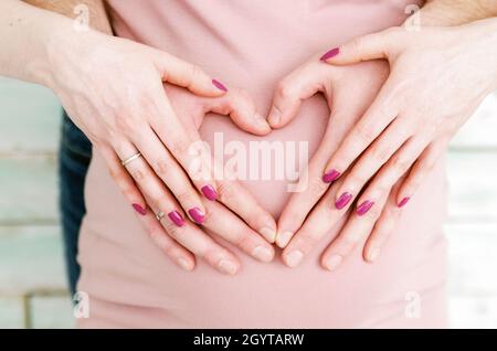 Schöne Schwangerin mit Bauch in rosa Kleid und Herz der Hände Stockfoto