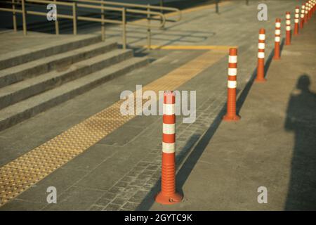 Parkposten in der Stadt. Schilder, die die Bewegung von Fahrzeugen einschränken. Orangefarbene weiße Warnhinweise halten an. Stockfoto