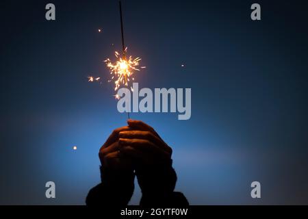 Menschliche Hände, die brennendes Feuer halten, funkeln. Wir feiern Neujahr, weihnachten oder Jubiläum. Hände halten brennendes Funkelfeuerwerk in der Nacht. Urlaub ce Stockfoto