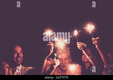 Familie feiert halten brennende funkelt mit erhobenen Armen. Eine Gruppe von Familien mit mehreren Generationen, die einen Geburtstag, ein Jubiläum oder ein neues Jahr feiern. Männer Stockfoto