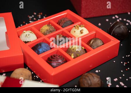 Verschiedene handgemachte Schokoladentrüffelkandys in einer roten Schachtel auf dunklem Grund. Nahaufnahme. Stockfoto