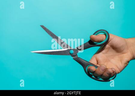 Hand mit farbenfroher Schere vor blauem Hintergrund mit Platz für Text und Designs. Stockfoto