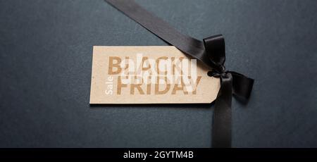 Schwarzer Friday Sale Text Schriftzug auf Preisschild, dunkler Hintergrund. Spezielle saisonale Angebote Schild, Kraftpapier braune Papierkarte und Satinband Schleife, Banner Stockfoto