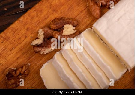 Geschnittene Kamembert- und Walnusskerne auf einem Holzschneidebrett, Nahaufnahme, selektiver Fokus Stockfoto