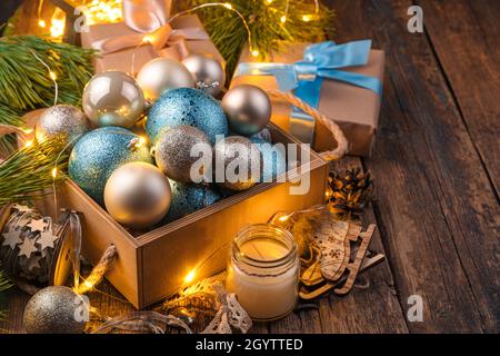 Eine Schachtel mit goldenen und blauen Weihnachtskugeln in Christbaumzweigen mit leuchtenden Lichtern. Das Konzept von Weihnachten und Neujahr. Stockfoto