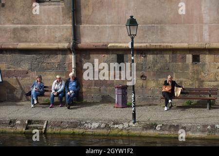 Menschen sitzen entspannt auf öffentlichen Sitzbänken am Fluss in Straßburg, Frankreich, 2021 Stockfoto