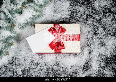 Dekoratives Weihnachtsgeschenk mit einem leeren Etikett im Schnee mit Schneeflocken auf Winterhintergrund. Stockfoto