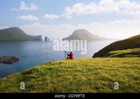 Der Wanderer genießt die wunderschöne Natur der Färöer-Inseln. Die Aussicht auf die Drangarnir-Meeresschächte und die Tindholmur-Insel von der landschaftlich reizvollen Straße aus Stockfoto