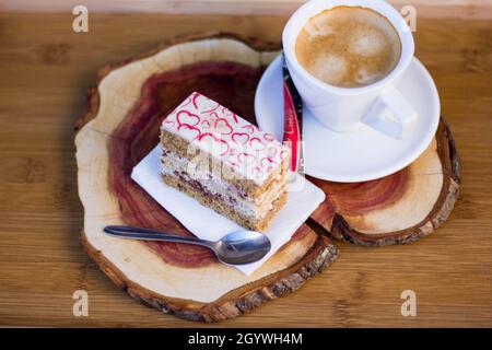 Leckere Tortenscheibe mit Cremefüllung und Herzdekor auf der Oberseite mit Kaffee auf dem Kirschtafel. Kaffeepause Stockfoto