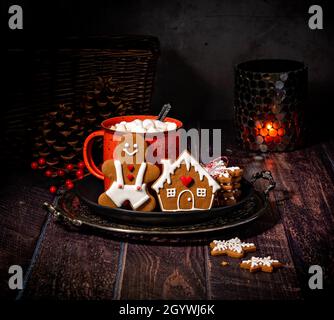 Rustikales und gemütliches weihnachtliches Ambiente im Winter. Heißer Kakao in einem roten Becher mit Salmmil und hausgemachten Lebkuchen. Stockfoto