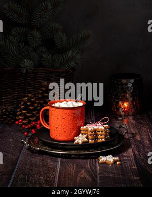 Rustikales und gemütliches weihnachtliches Ambiente im Winter. Heißer Kakao in einem roten Becher mit Salmmil und hausgemachten Lebkuchen. Stockfoto