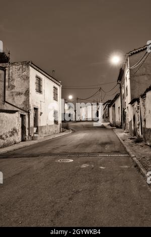 Vertikale Aufnahme einer Landstraße mit alten Steinhäusern auf beiden Seiten. Low-Angle-Shot-Graustufen Stockfoto