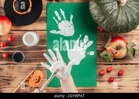 Schritt-für-Schritt Halloween Tutorial Geister Kinder Handprint. Schritt 5: Das Kind trägt mit dem Pinsel weiße Farbe auf die Handfläche auf. Draufsicht Stockfoto