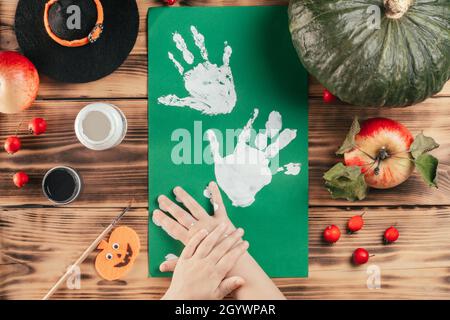 Schritt-für-Schritt Halloween Tutorial Geister Kinder Handprint. Schritt 6: Das Kind hinterlässt einen Handflächendruck auf einem farbigen Papier. Draufsicht Stockfoto