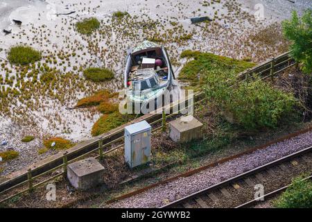 Von einem hohen conwy-Burgturm aus blickt man auf ein kleines Boot, das sich auf dem Gezeitenwasserstrasse neben einer Bahnlinie, Conwy Wales, auf Schlamm ruhte Stockfoto