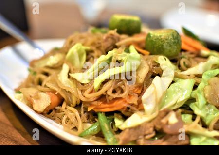 Unter heißem Rühren Nudeln mit Gemüse, Fleisch, Meeresfrüchten und Calamansi auf einem weißen Teller anbraten Stockfoto