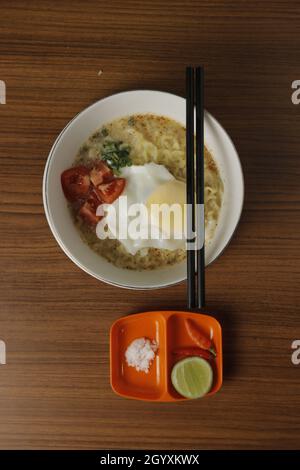 Nudelsuppe mit Eiern, Tomaten und grünen Zwiebeln, serviert mit Chilisauce und Limette als Ergänzung. Stockfoto