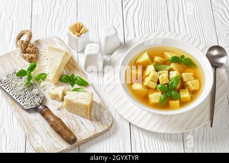 Zuppa imperiale, italienische Suppe aus Hühnerbrühe mit Parmesan-Eierknödeln, bestreut mit geriebenem Käse und Basilikum in einer Schüssel auf einem Holztisch Stockfoto