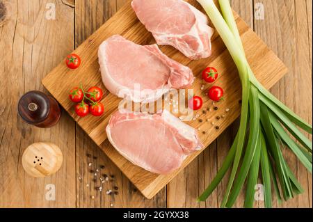 Frische Steaks aus ausgesuchter Fleischsorte auf einem Holzbrett mit Gemüse und Gewürzen. Draufsicht Stockfoto