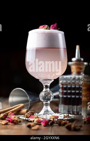 Weibliche rosa Cocktail mit Schaum in einem Glas. Dekoriert mit getrockneten Rose. Im Hintergrund ist sichtbar Barkeeper Inventar Stockfoto