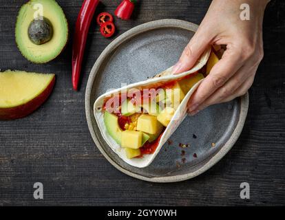 Mexikanische Tacos in menschlicher Hand auf dunklem Holztisch, Draufsicht Stockfoto