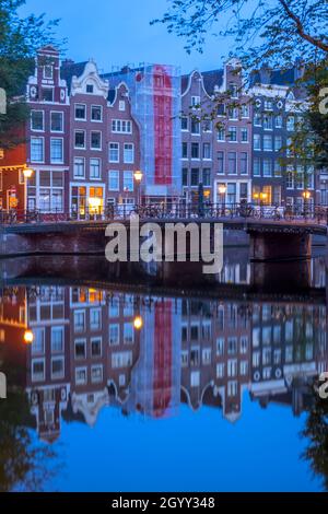 Niederlande. Am frühen Morgen in Amsterdam. Brücke mit geparkten Fahrrädern und Reflexionen von traditionellen Häusern im Wasser des Kanals Stockfoto