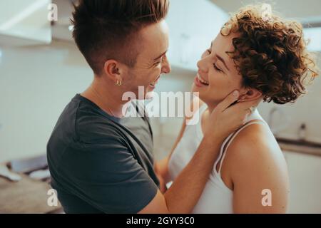Liebhaber lachen in der Küche. Zwei romantische junge queere Liebhaber lachen fröhlich, während sie einander angucken. Fröhliche junge LGBTQ+ Paar mit f Stockfoto