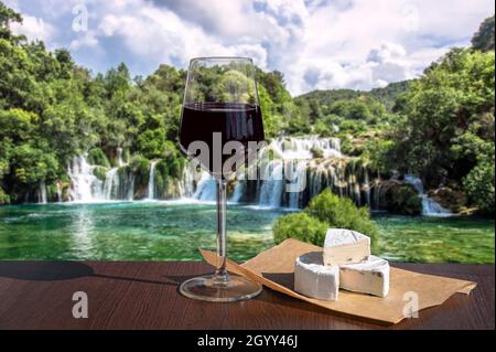 Ein Glas Rotwein mit Käsesnacks gegen die Wasserfall-Kaskade im Wald. Stockfoto