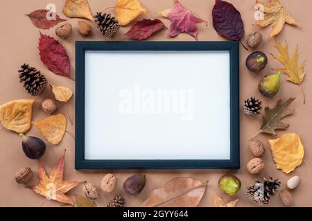 Herbst flach legen mit Blättern, Feigen, Walnüssen und Zapfen auf hellbraunem Hintergrund. Leerer Bilderrahmen in der Mitte. Mock-up, Draufsicht, Kopierbereich. Stockfoto