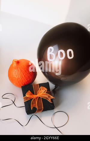 Geschenk in einer Schachtel, orangefarbener hokkaido-Kürbis, schwarzer Ballon mit Wort Boo auf weißem Hintergrund. Halloween-Konzept. Stockfoto