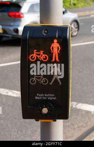 Ein Fußgängerübergangssignal auf der roten „Don't Cross“ neben einer viel befahrenen Straße mit einer Autoüberquerung im Hintergrund in Basingstoke, Großbritannien Stockfoto