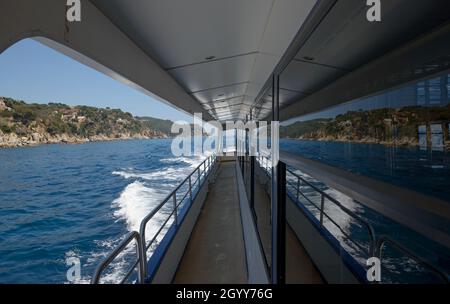 Blick auf Trimaran Deck mit schäumenden Pfad achteraus und Spiegelung der Costa Brava Küste, Katalonien. Stockfoto