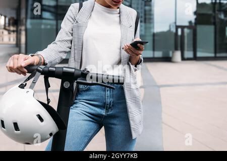 Nicht erkennbare Geschäftsfrau im Bürogebäude mit Elektroroller halten Smartphone stehen Stockfoto