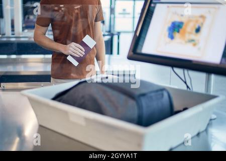 Sicherheitskontrolle am Flughafen. Junger Mann, der auf die Röntgenkontrolle seiner Tasche wartet. Stockfoto