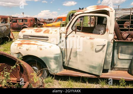 Ein Feld mit alten, verrosteten Lkws und Autos unter blauem Himmel mit Wolken, die alte Fahrzeuge auf einem Schrottplatz präsentieren. Stockfoto