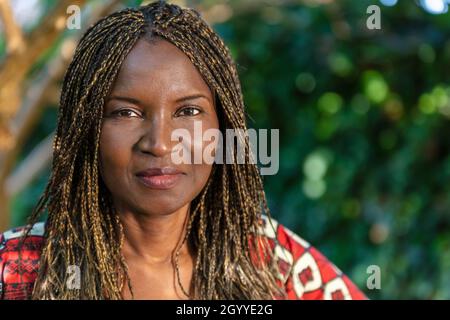 Attraktive afrikanische oder afroamerikanische Frau mittleren Alters, weiblich in Afrika, mit geflochtenen Haaren in Zöpfen, in traditioneller Kleidung Stockfoto