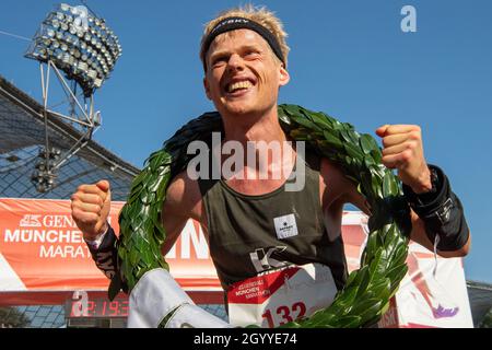 München, Deutschland. Oktober 2021. Alexander Hirschhäuser trägt einen Lorbeerkranz und jubelt nach dem Sieg beim Münchner Marathon 2021 im Olympiastadion. Er lief in 2:18:38 Stunden bei kalten Temperaturen knapp über dem Gefrierpunkt zum Titel. Kredit: Peter Kneffel/dpa/Alamy Live Nachrichten Stockfoto