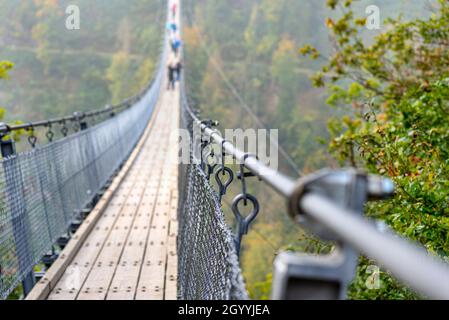 Hängebrücke aus Holz mit Stahlseilen über einem dichten Wald in Westdeutschland, Nahaufnahme eines Handlaufs aus Seil. Stockfoto