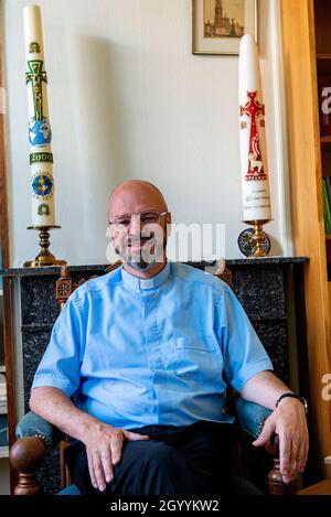 Tilburg, Niederlande. Wohnzimmer Porträt eines 56-jährigen katholischen Priesters, der auf seinem Lesestuhl sitzt und sich geistig und geistlich auf seine neue kommission vorbereitet, die ihm sein Bischof gegeben hat. Stockfoto